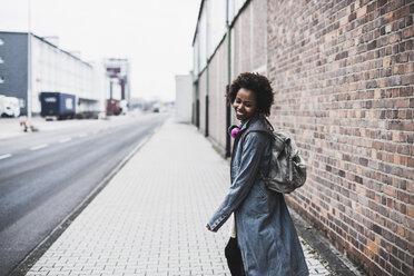 Smiling young woman with headphones and backpack on pavement - UUF09787