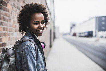 Portrait of smiling young woman with headphones and backpack - UUF09788