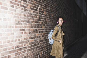 Young woman standing in front of brick wall listening music with headphones - UUF09800