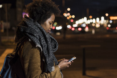 Junge Frau überprüft ihr Smartphone am Straßenrand - UUF09803