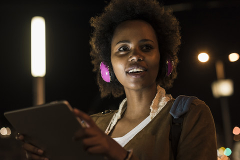 Porträt einer jungen Frau mit Kopfhörern und Tablet bei Nacht, lizenzfreies Stockfoto