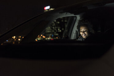 Lächelnde junge Frau, die nachts in einem Auto sitzt und ein Tablet benutzt - UUF09820