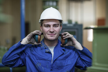 Porträt eines Arbeiters mit Helm und Ohrenschützern in einer Fabrik - ZEF12402