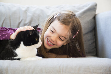 Porträt eines glücklichen kleinen Mädchens, das auf der Couch liegt und eine Katze streichelt - LVF05787