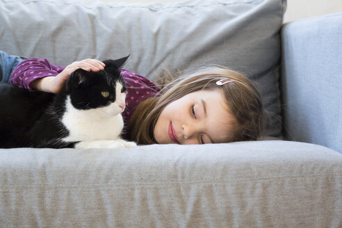 Kleines Mädchen liegt auf der Couch und streichelt eine Katze - LVF05788