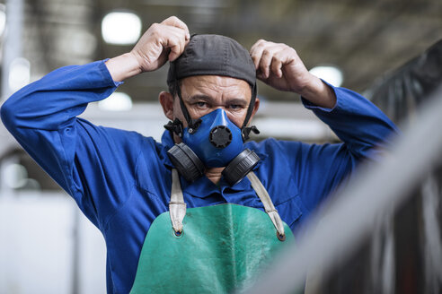 Arbeiter beim Anlegen einer Atemschutzmaske in einer Fabrik - ZEF12424