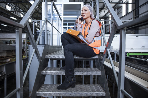 Inspektorin am Telefon auf einer Treppe in einer Fabrik sitzend, lizenzfreies Stockfoto