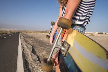 Spanien, Teneriffa, junge Frau mit Skateboard steht an leerer Landstraße, Teilansicht - SIPF01336