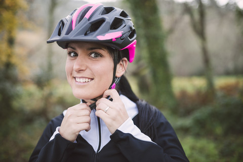 Porträt einer lächelnden Frau, die einen Fahrradhelm aufsetzt, lizenzfreies Stockfoto