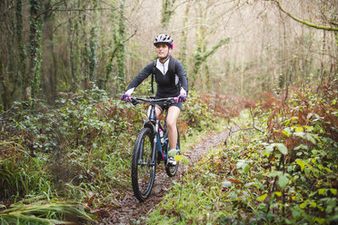 Mountainbikerin fährt mit ihrem Fahrrad auf einem Waldweg - RAEF01661