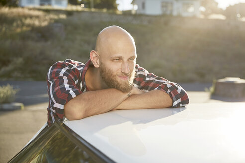 Porträt eines glatzköpfigen jungen Mannes mit Bart, der sich auf ein Autodach stützt - SRYF00217