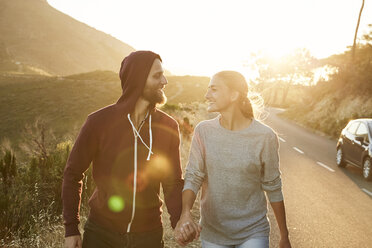 South Africa, Cape Town, happy young couple walking hand in hand at roadside - SRYF00237