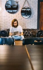 Stylish young man sitting on couch in a cafe using tablet - MGOF02811