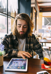 Stilvoller junger Mann, der in einem Café ein Tablet betrachtet - MGOF02815