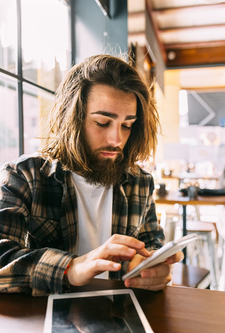 Stilvoller junger Mann benutzt Handy in einem Café, lizenzfreies Stockfoto