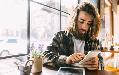 Stilvoller junger Mann benutzt Handy in einem Café - MGOF02818