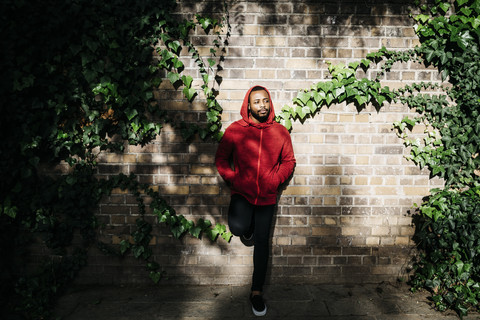 Junger Mann mit rotem Kapuzenpulli lehnt an einer Wand, lizenzfreies Stockfoto