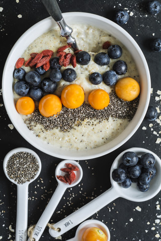 Schüssel Porridge mit Milch, Blaubeeren, Chia, Physalis und Gojibeeren, lizenzfreies Stockfoto