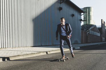 Junger Geschäftsmann fährt Skateboard auf der Straße - UUF09822