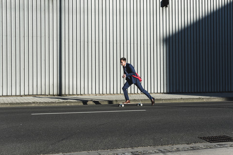 Junger Geschäftsmann fährt Skateboard auf der Straße, lizenzfreies Stockfoto