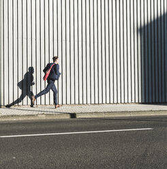 Young businessman running on pavement along building - UUF09828