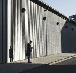 Young businessman standing on pavement looking at cell phone - UUF09831