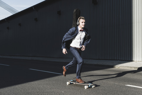 Junger Mann mit Gitarrenkoffer fährt Skateboard auf der Straße, lizenzfreies Stockfoto