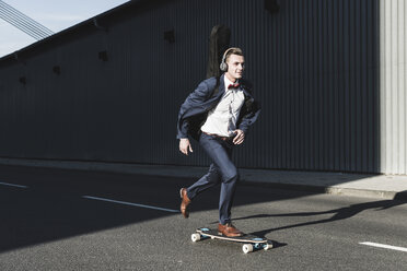 Junger Mann mit Gitarrenkoffer fährt Skateboard auf der Straße - UUF09833