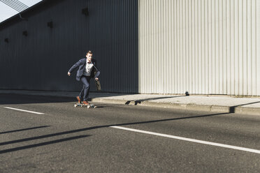 Junger Geschäftsmann fährt Skateboard auf der Straße - UUF09840