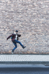 Young man jumping in front of brick wall - UUF09844