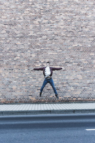 Junger Mann springt vor eine Ziegelmauer, lizenzfreies Stockfoto