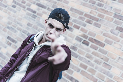 Portrait of young man gesturing in front of brick wall stock photo