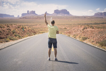 USA, Utah, Rückenansicht eines Mannes, der auf der Straße zum Monument Valley steht und das Siegeszeichen zeigt - EPF00273