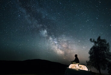 Österreich, Mondsee, Silhouette eines auf dem Autodach sitzenden Mannes unter Sternenhimmel - WVF00790