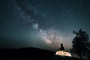 Austria, Mondsee, silhouette of man sitting on car roof under starry sky - WVF00790