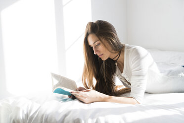 Junge Frau liegt auf dem Bett und liest ein Buch - KKAF00314