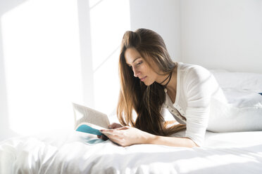 Young woman lying on bed reading book - KKAF00314