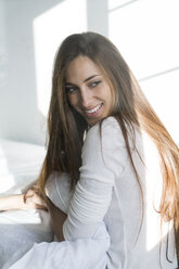 Smiling young woman sitting on bed - KKAF00324