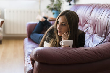Junge Frau liegt auf der Couch und hält eine Tasse Kaffee - KKAF00339
