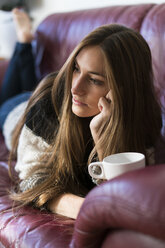 Junge Frau auf der Couch liegend mit einer Tasse Kaffee - KKAF00340