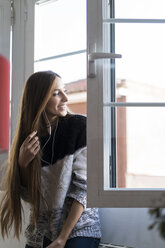 Lächelnde junge Frau mit Kopfhörern, die aus dem Fenster schaut - KKAF00343