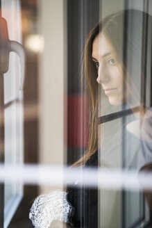 Ernste junge Frau schaut aus dem Fenster - KKAF00356