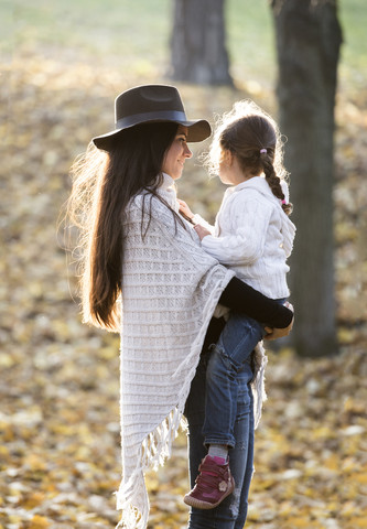 Mutter trägt ihre Tochter im herbstlichen Wald, lizenzfreies Stockfoto