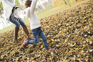 Girl running with mother in autumnal leaves - HAPF01318