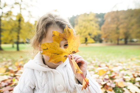 Mädchen schaut durch ein Loch im Herbstblatt, lizenzfreies Stockfoto