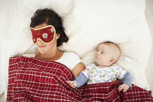 Mutter mit Schlafmaske und wachem Baby im Bett liegend - FSF00654