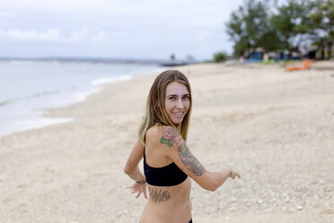 Indonesien, Bali, lächelnde Frau mit Tattoos am Strand - KNTF00618