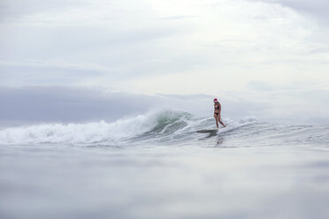 Indonesien, Bali, Frau mit Weihnachtsmannmütze beim Surfen auf einer Welle - KNTF00622