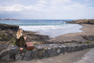 Spanien, Teneriffa, junge blonde Frau sitzt auf einer Mauer in der Nähe des Strandes - SIPF01344