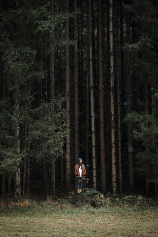 Junger Mann steht vor einem Nadelwald, lizenzfreies Stockfoto